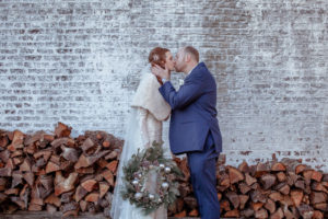 Bride kissing her groom holding a winter wreath